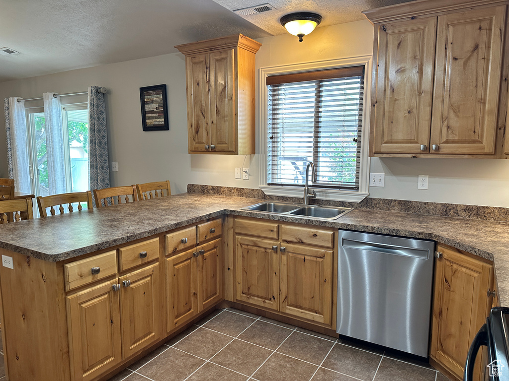 Kitchen with stainless steel dishwasher, a sink, dark countertops, dark tile patterned flooring, and a peninsula