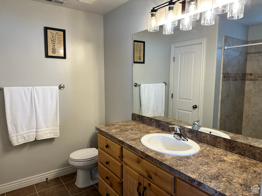 Full bathroom with vanity, tile patterned floors, tiled shower, toilet, and baseboards