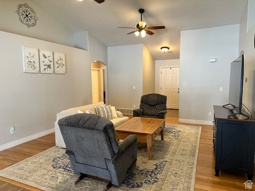 Living area featuring arched walkways, ceiling fan, light wood-style floors, baseboards, and vaulted ceiling