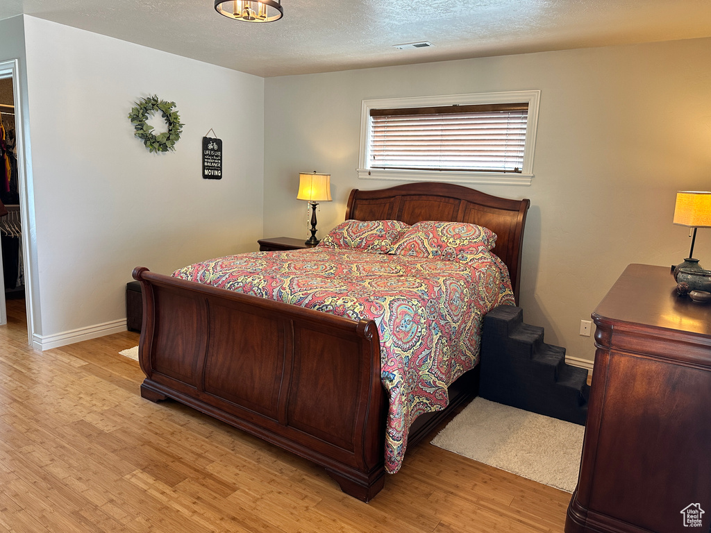 Bedroom featuring light wood finished floors, baseboards, a spacious closet, a textured ceiling, and a closet