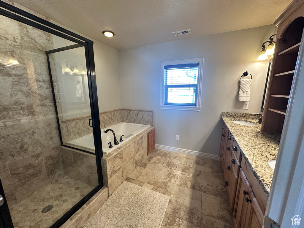 Full bathroom featuring a garden tub, a shower stall, double vanity, baseboards, and stone finish floors
