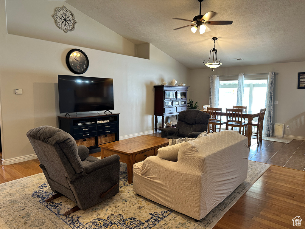 Living area with lofted ceiling, ceiling fan, baseboards, a textured ceiling, and wood finished floors