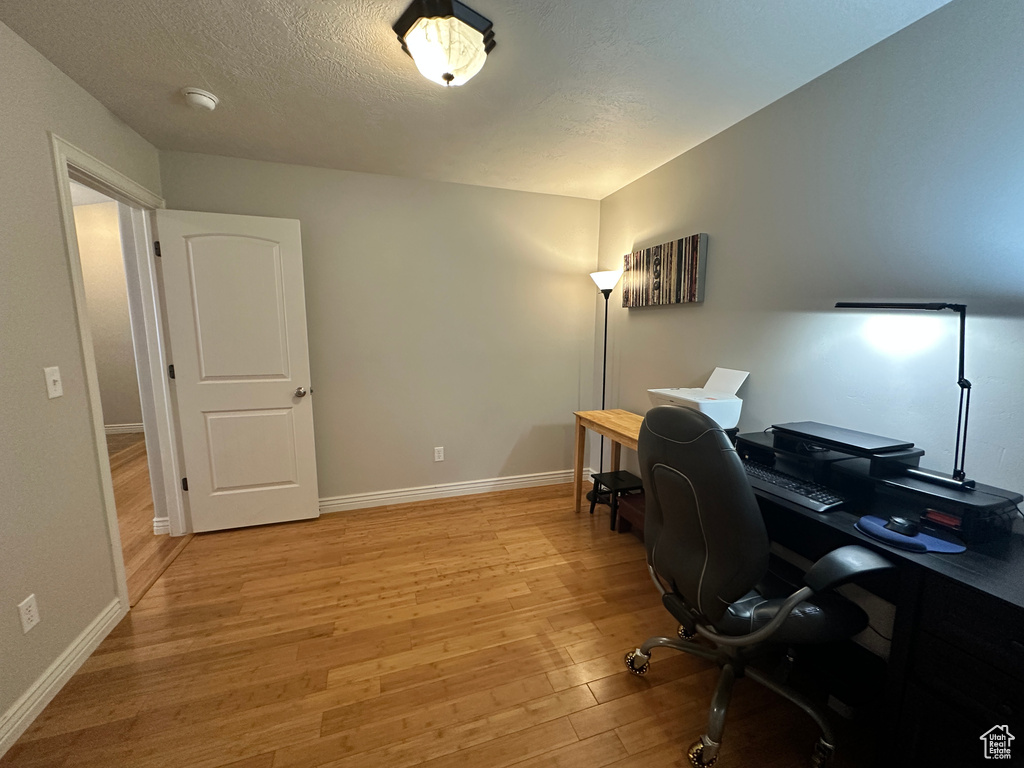 Office with light wood finished floors, baseboards, and a textured ceiling