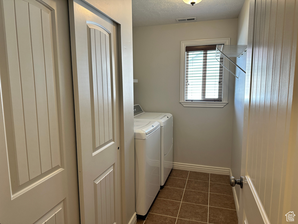 Washroom featuring separate washer and dryer, dark tile patterned flooring, baseboards, and a textured ceiling