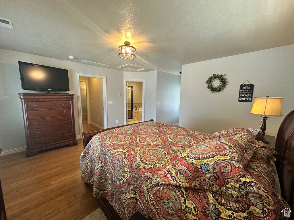 Bedroom featuring wood finished floors, baseboards, ensuite bathroom, and a textured ceiling