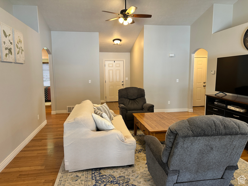 Living room with arched walkways, a ceiling fan, light wood-style floors, and baseboards