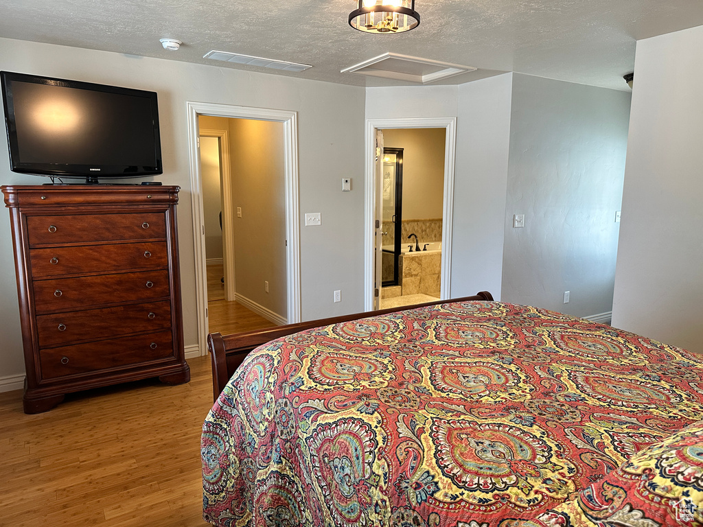 Bedroom with wood finished floors, a textured ceiling, baseboards, connected bathroom, and attic access