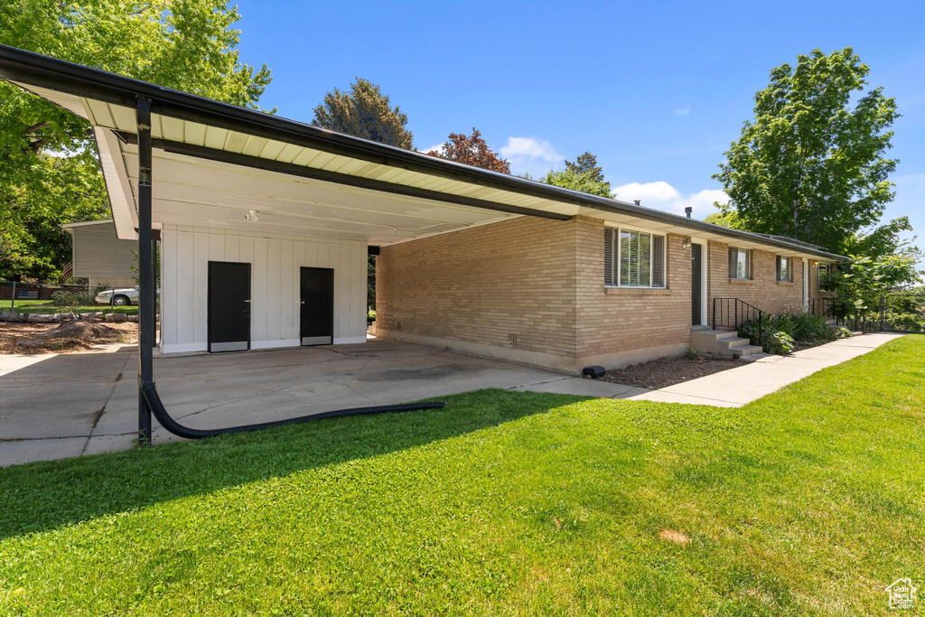 Rear view of property featuring brick siding, an attached carport, a yard, and driveway