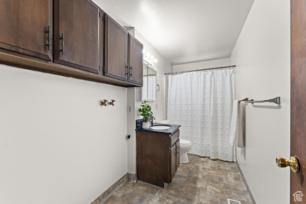 Bathroom featuring stone finish flooring, vanity, toilet, baseboards, and curtained shower