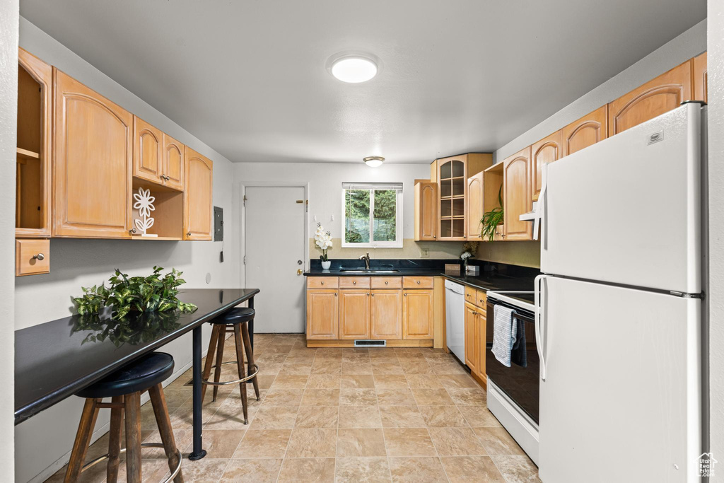 Kitchen featuring white appliances, a sink, open shelves, dark countertops, and light brown cabinetry