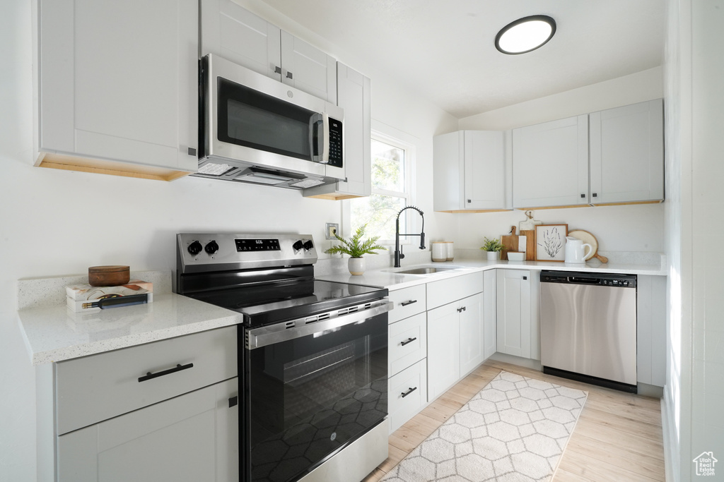 Kitchen with stainless steel appliances, a sink, light wood-style flooring, and white cabinetry
