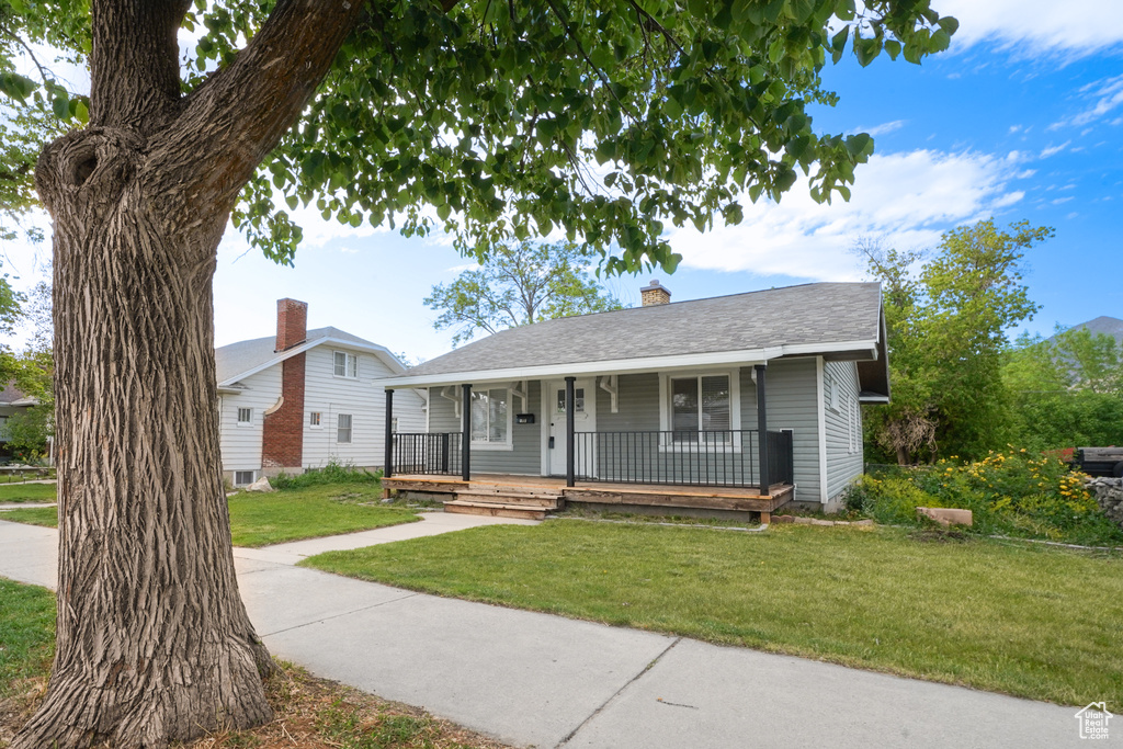 View of front of home featuring a porch, a front lawn, a chimney, and a shingled roof