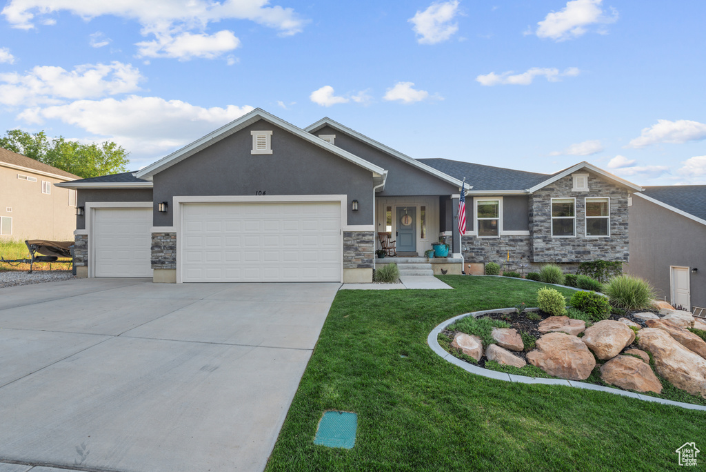 View of front of home featuring stucco siding, an attached garage, stone siding, a front yard, and driveway