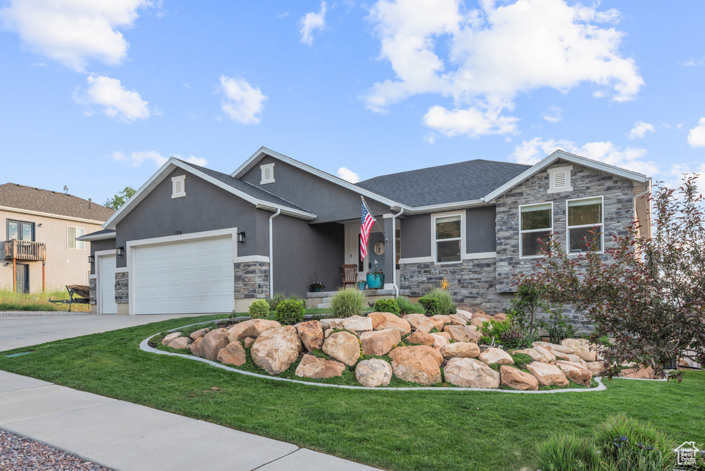 View of front facade featuring stone siding, stucco siding, a garage, and a front yard