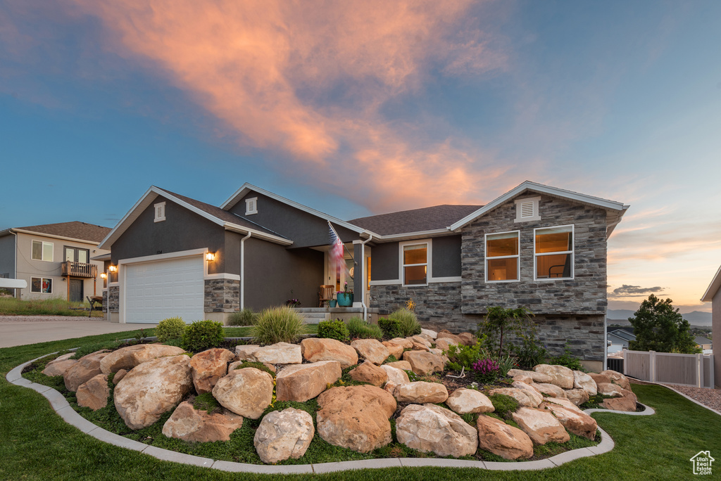 View of front facade featuring stone siding, stucco siding, a garage, and driveway