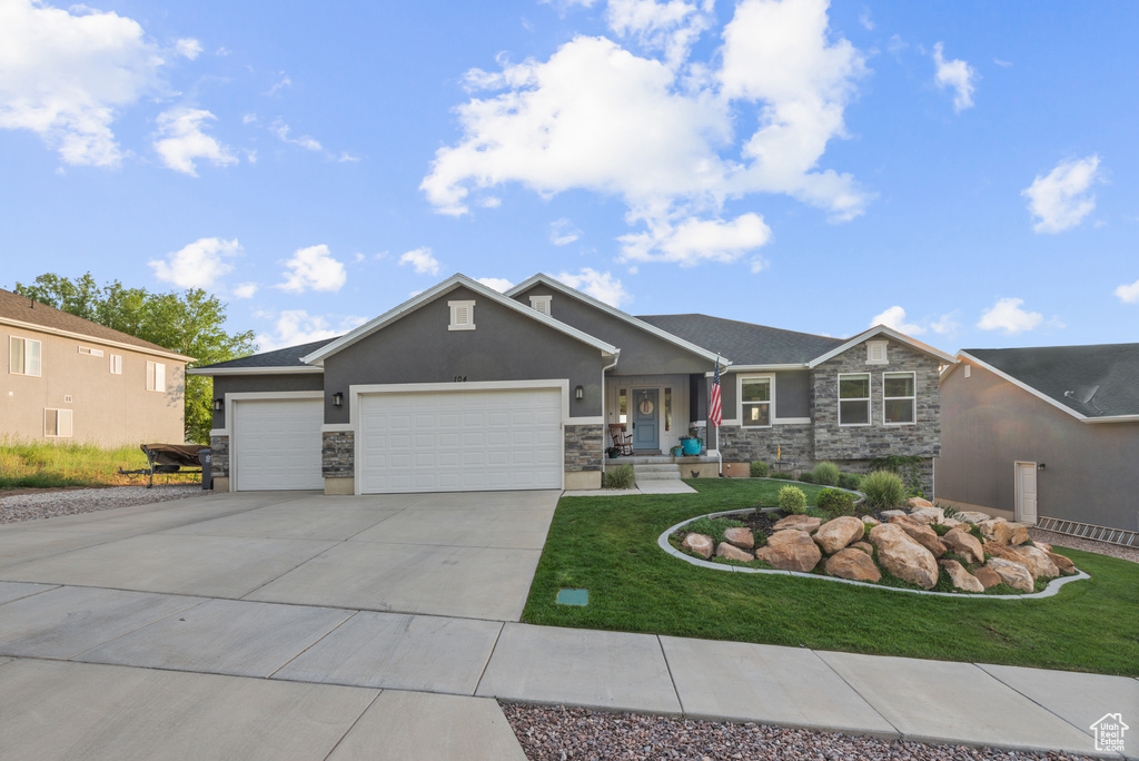 View of front of home featuring stone siding, an attached garage, driveway, stucco siding, and a front yard