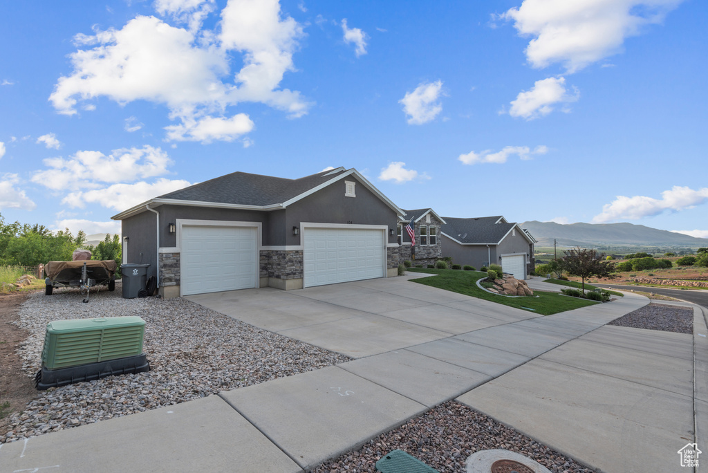 View of side of property with a garage, stucco siding, stone siding, driveway, and a mountain view