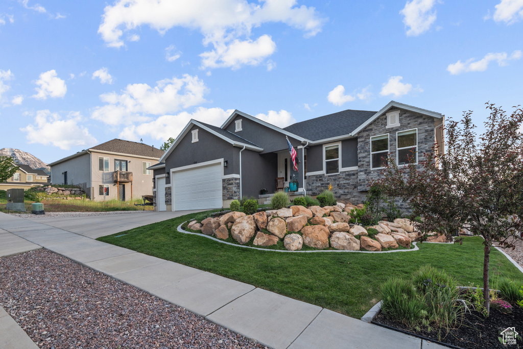 View of front of property featuring stone siding, driveway, a front lawn, an attached garage, and stucco siding