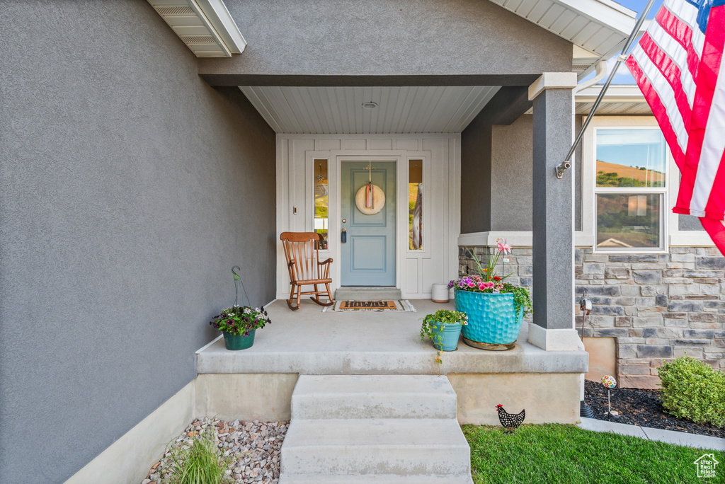 Doorway to property with stucco siding, stone siding, and covered porch