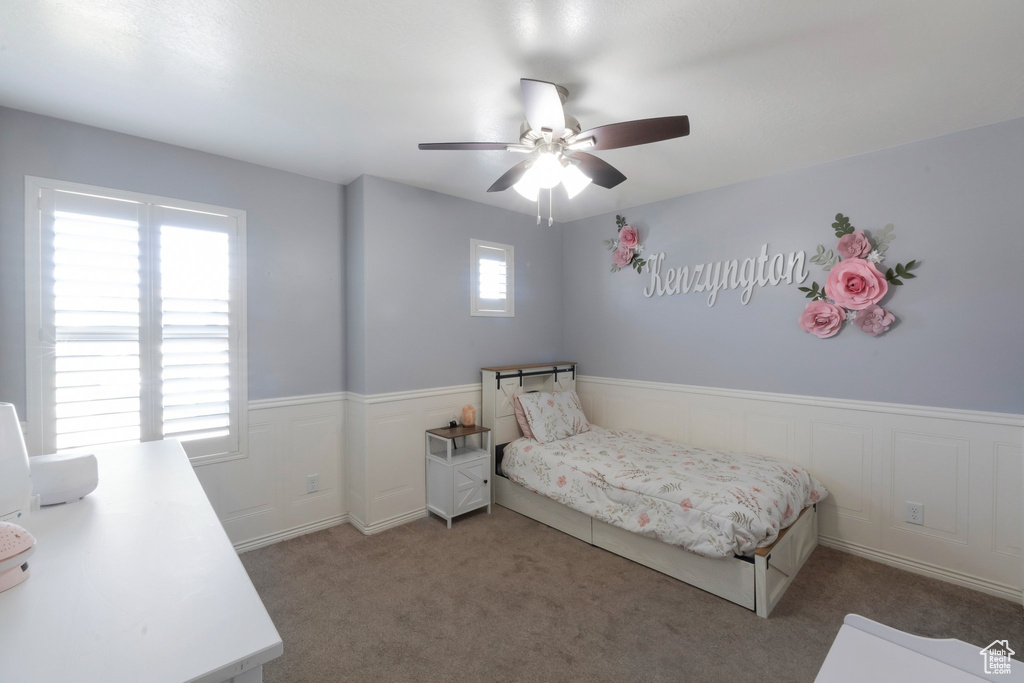 Carpeted bedroom featuring wainscoting and a ceiling fan
