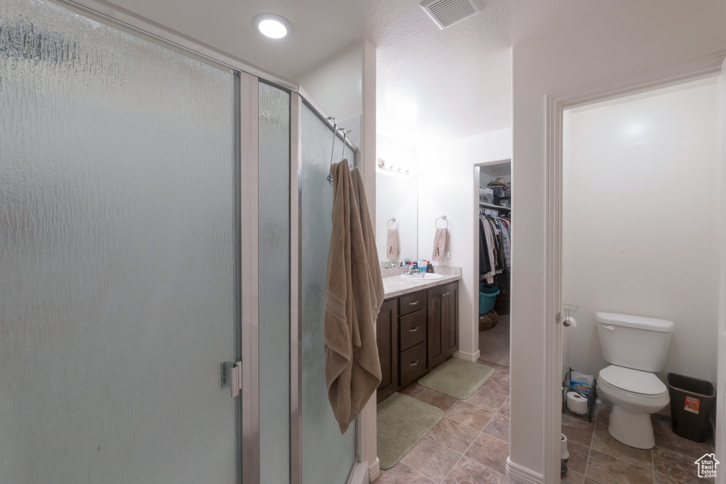 Bathroom featuring a shower stall, toilet, a walk in closet, vanity, and tile patterned floors