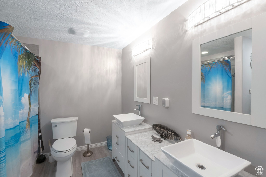 Bathroom featuring double vanity, a textured ceiling, wood finished floors, toilet, and curtained shower