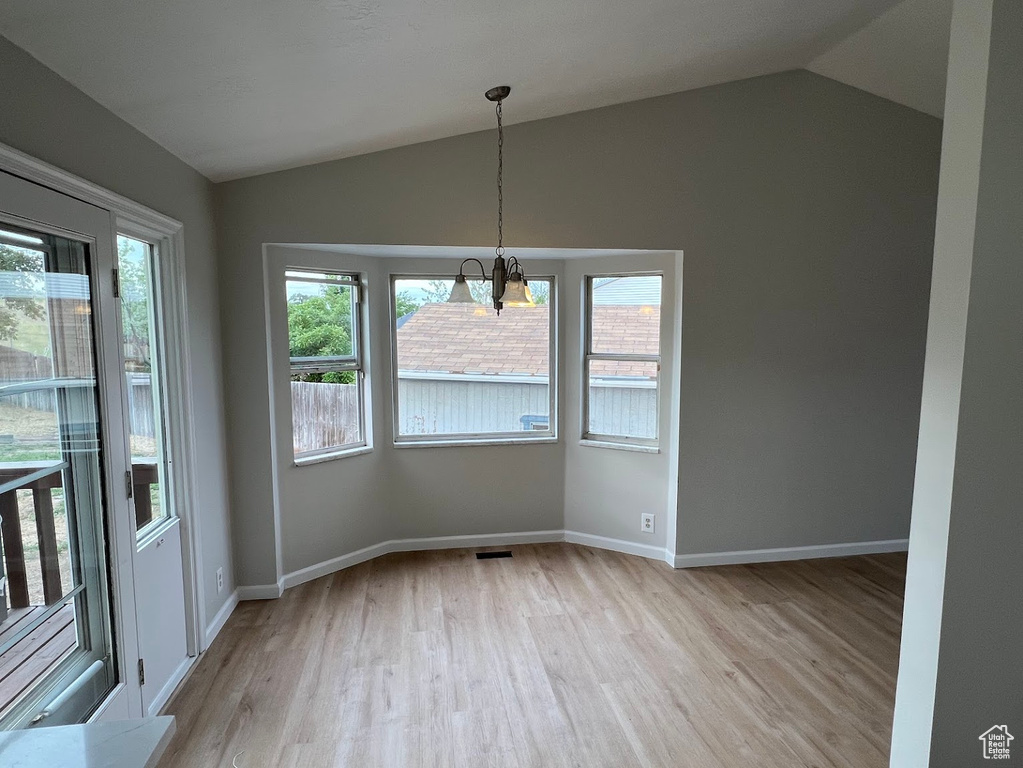 Unfurnished dining area with lofted ceiling, light wood-style floors, baseboards, and a chandelier