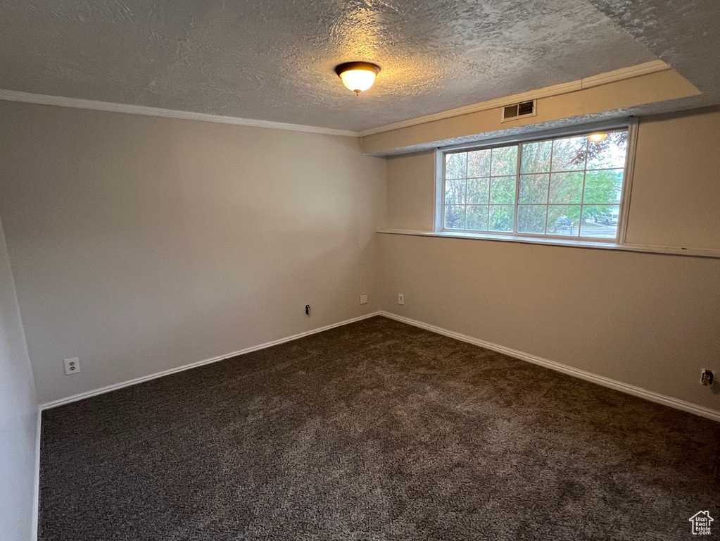 Spare room featuring dark carpet, baseboards, a textured ceiling, and crown molding