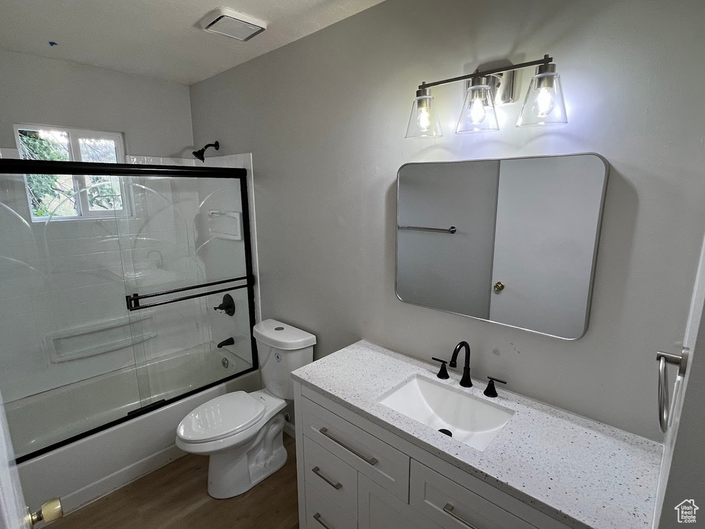 Bathroom featuring toilet, shower / bath combination with glass door, vanity, and wood finished floors