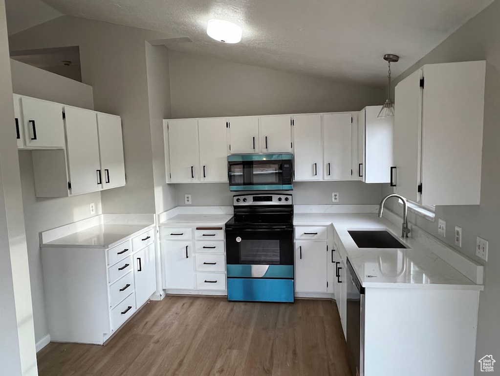 Kitchen featuring range with electric stovetop, a sink, lofted ceiling, wood finished floors, and white cabinets