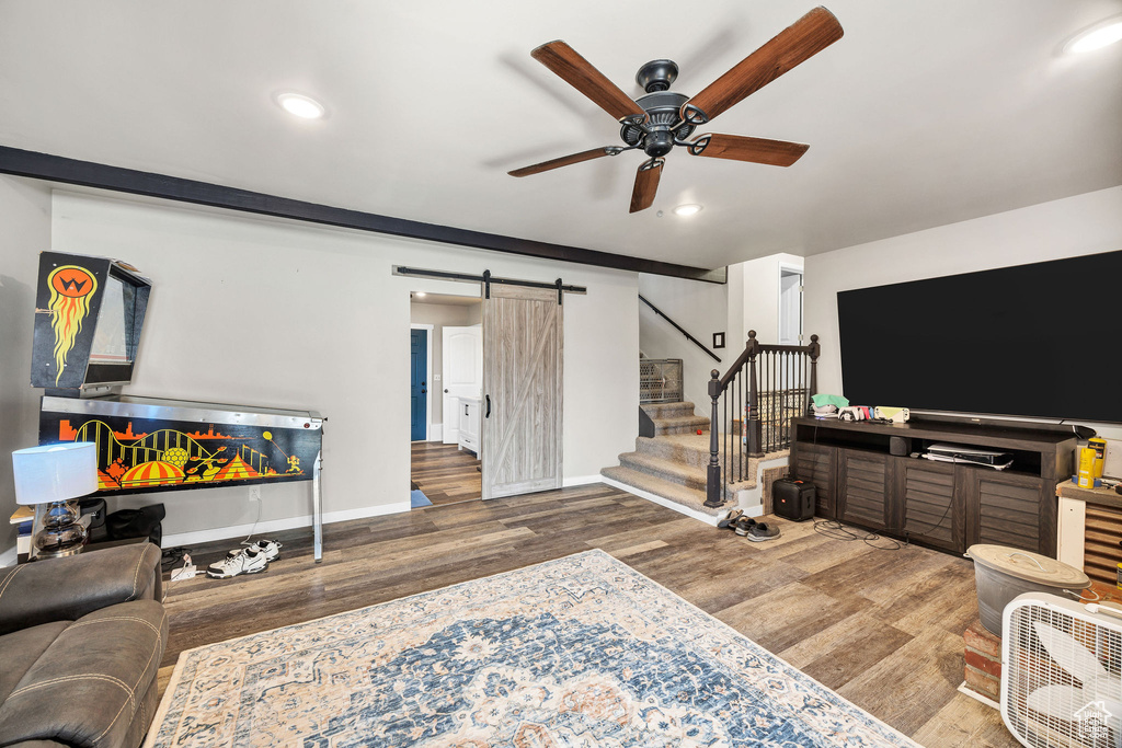 Living room featuring a barn door, a ceiling fan, wood finished floors, stairs, and baseboards