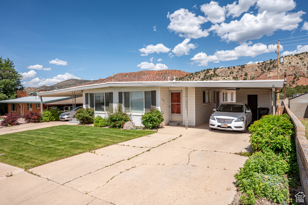 View of front of home with concrete driveway, an attached carport, a front yard, and a mountain view