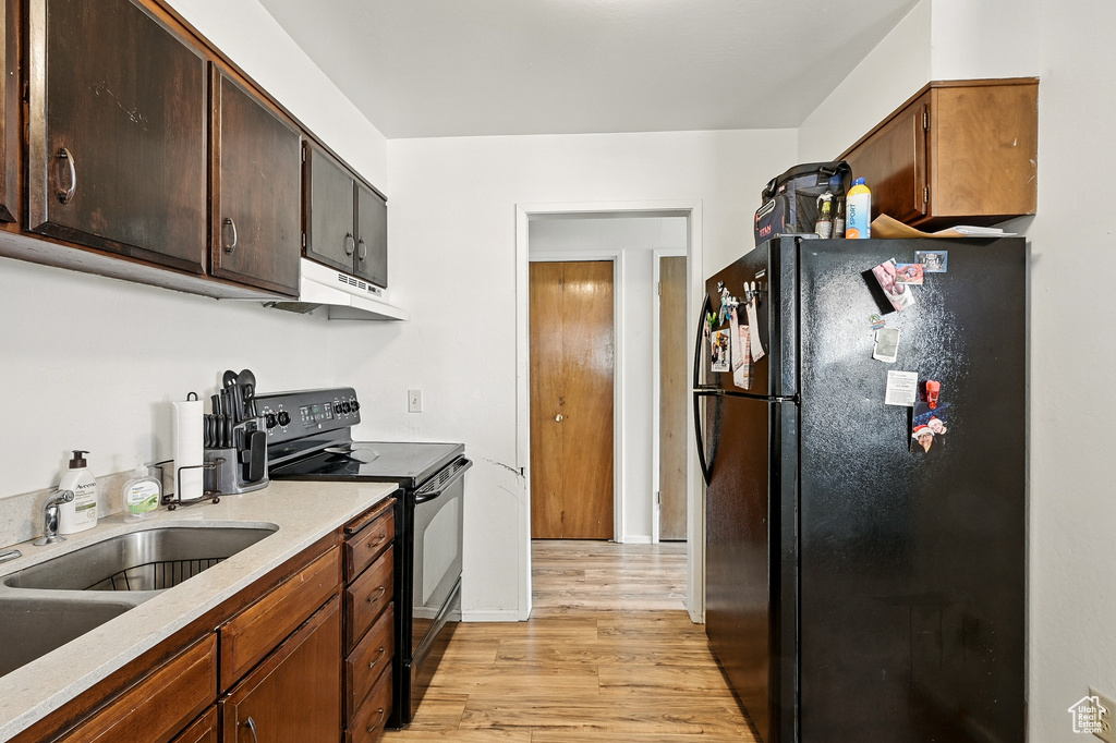 Kitchen featuring black appliances, under cabinet range hood, light wood-type flooring, a sink, and light countertops
