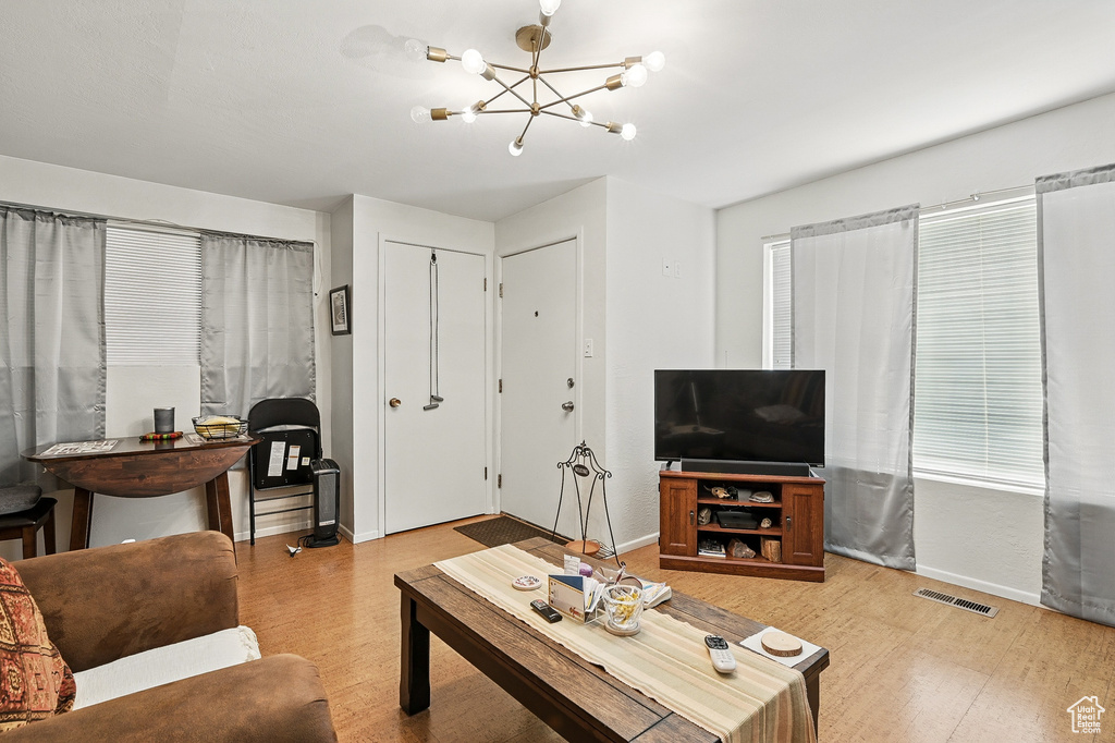 Living area with light wood-type flooring, baseboards, a chandelier, and healthy amount of natural light