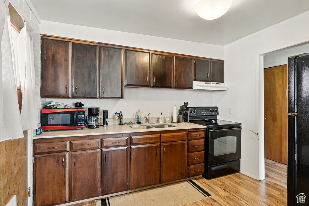 Kitchen with black appliances, a sink, under cabinet range hood, light wood-type flooring, and light countertops
