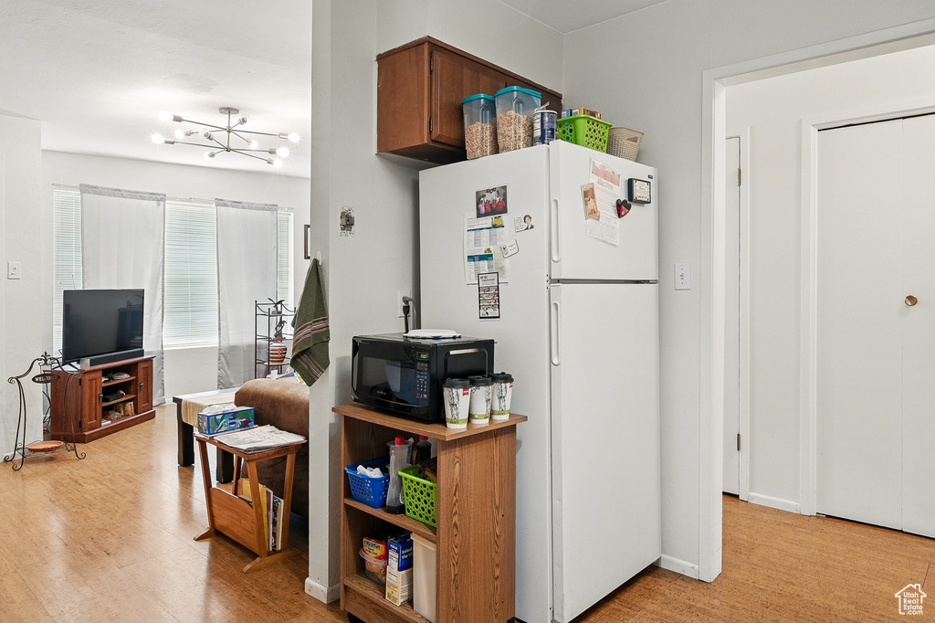 Kitchen featuring black microwave, freestanding refrigerator, a chandelier, and light wood-style floors