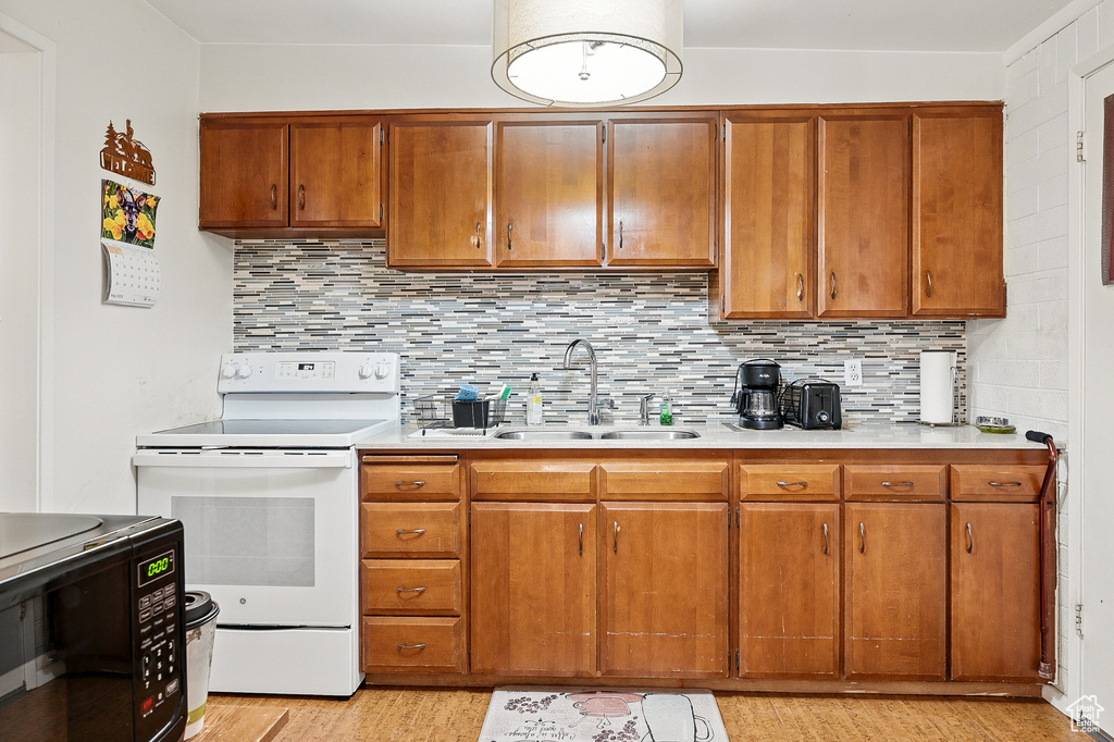 Kitchen with electric range, a sink, light wood-style flooring, light countertops, and backsplash