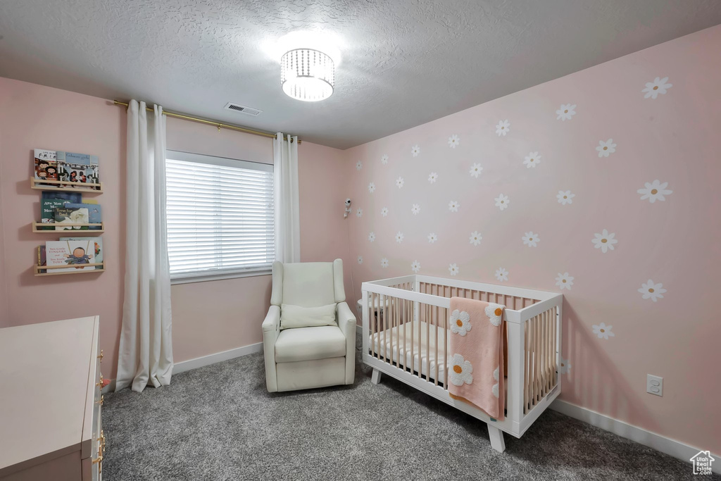 Carpeted bedroom with a textured ceiling, baseboards, and a nursery area