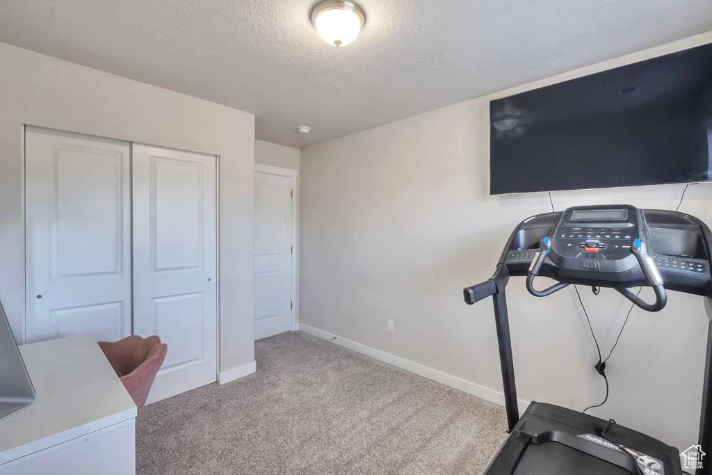 Exercise room with a textured ceiling, carpet, and baseboards