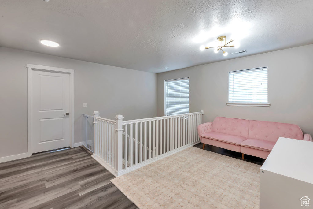 Sitting room with wood finished floors, a textured ceiling, baseboards, and an upstairs landing