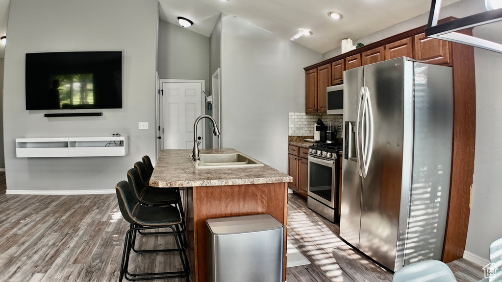 Kitchen with appliances with stainless steel finishes, a sink, wood finished floors, decorative backsplash, and vaulted ceiling