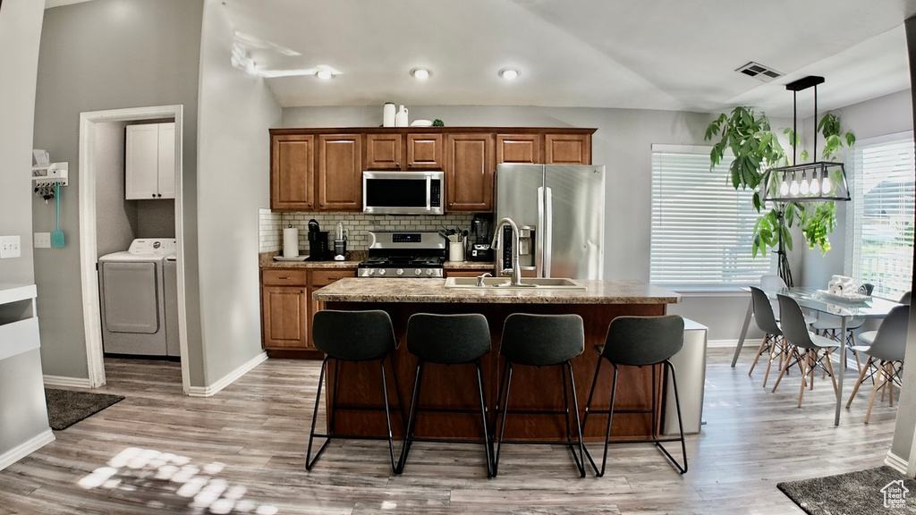 Kitchen featuring appliances with stainless steel finishes, a sink, baseboards, a breakfast bar, and vaulted ceiling