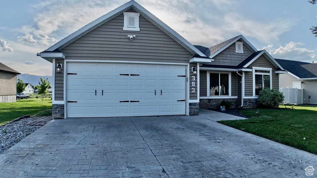 Single story home featuring decorative driveway, stone siding, a front yard, and a garage