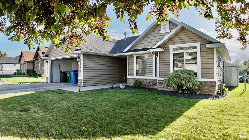 View of front of home featuring stone siding, asphalt driveway, a front yard, a garage, and roof with shingles