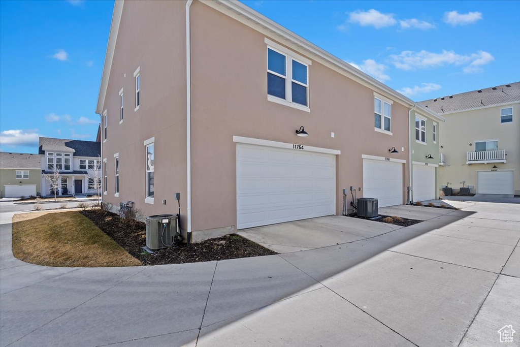 View of home's exterior with stucco siding, an attached garage, central air condition unit, and concrete driveway