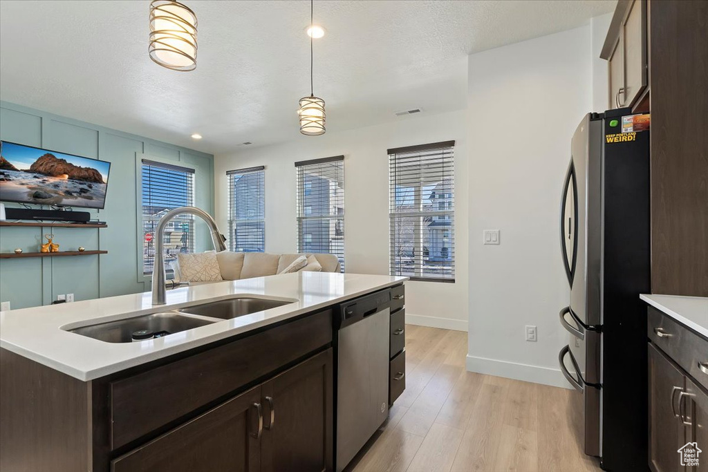 Kitchen featuring stainless steel appliances, a sink, dark brown cabinets, light countertops, and light wood-type flooring