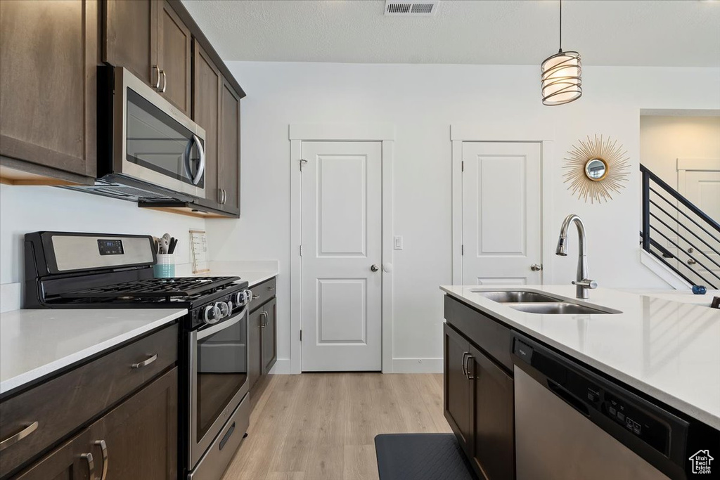 Kitchen featuring appliances with stainless steel finishes, a sink, light wood-style flooring, and light countertops