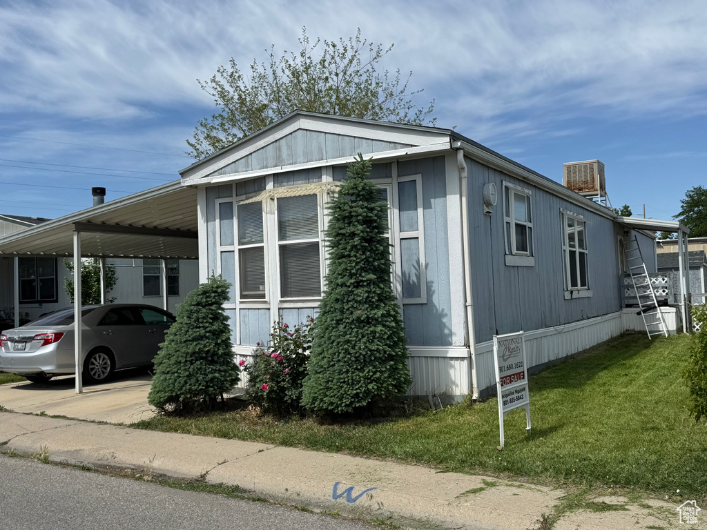 View of side of property with an attached carport, a lawn, and central AC