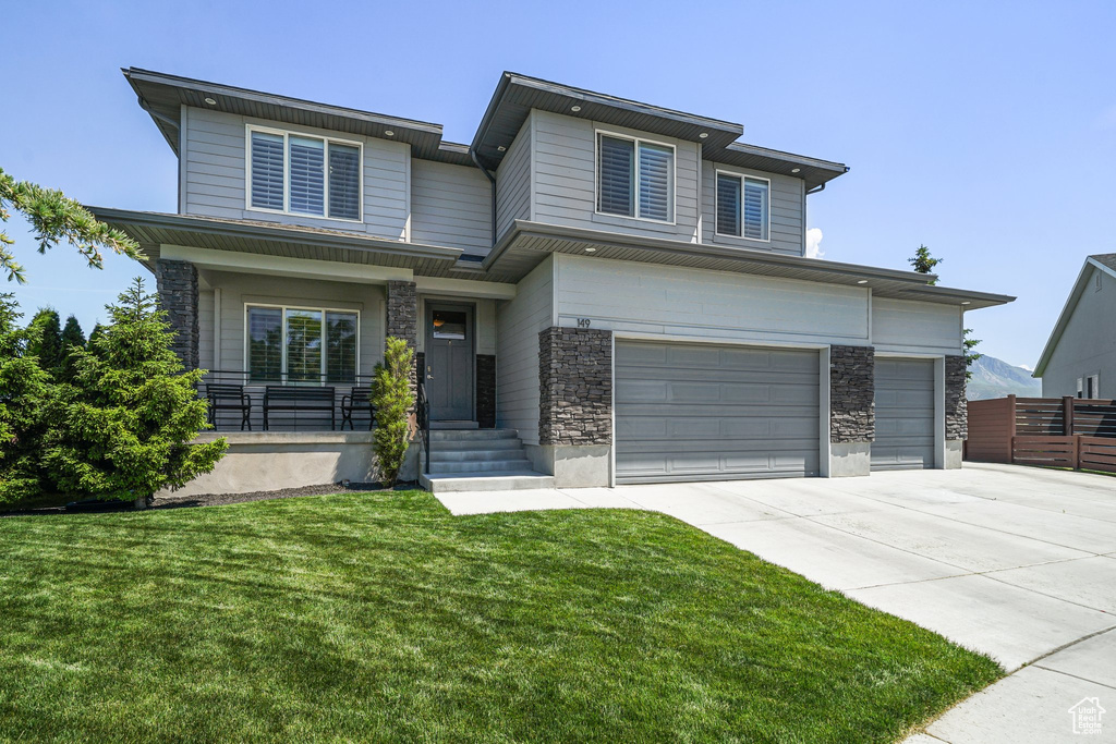 View of front facade with driveway, stone siding, an attached garage, and a porch