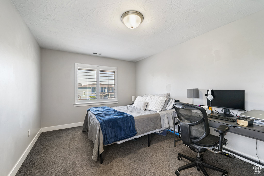 Bedroom with an office area, carpet floors, baseboards, and a textured ceiling